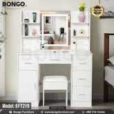 A promotional image of a modern white vanity set from BONGO, shown in a bedroom. The dressing table features a large central mirror with an integrated LED light, flanked by small shelves. The base includes multiple handleless drawers and a cabinet, with a matching white stool tucked underneath. A "Highest Quality" seal is in the top corner.